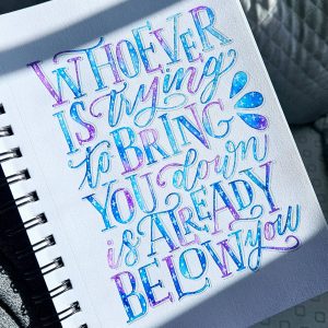 Hand‑lettered quote reading “Whoever is trying to bring you down is already below you” painted in blue and purple