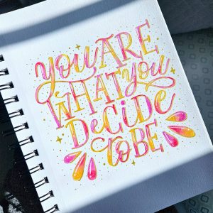 Hand‑lettered quote reading “You are what you decide to be” painted in orange and magenta